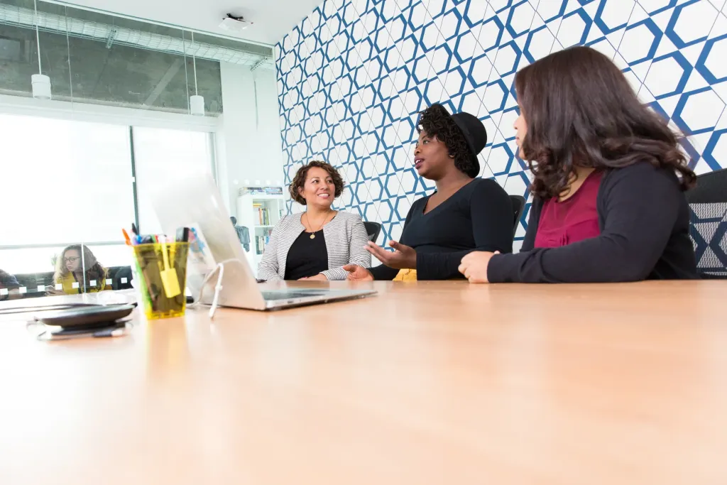 Three colleagues discussing their work around a table with an open laptop
